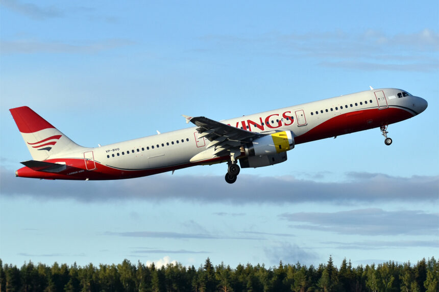 An Avolon Airbus A321-231 aircraft taking off of the runway. The livery on the aircraft is red and spells out 'Kings'. The sky is bright blue and clear in the background.