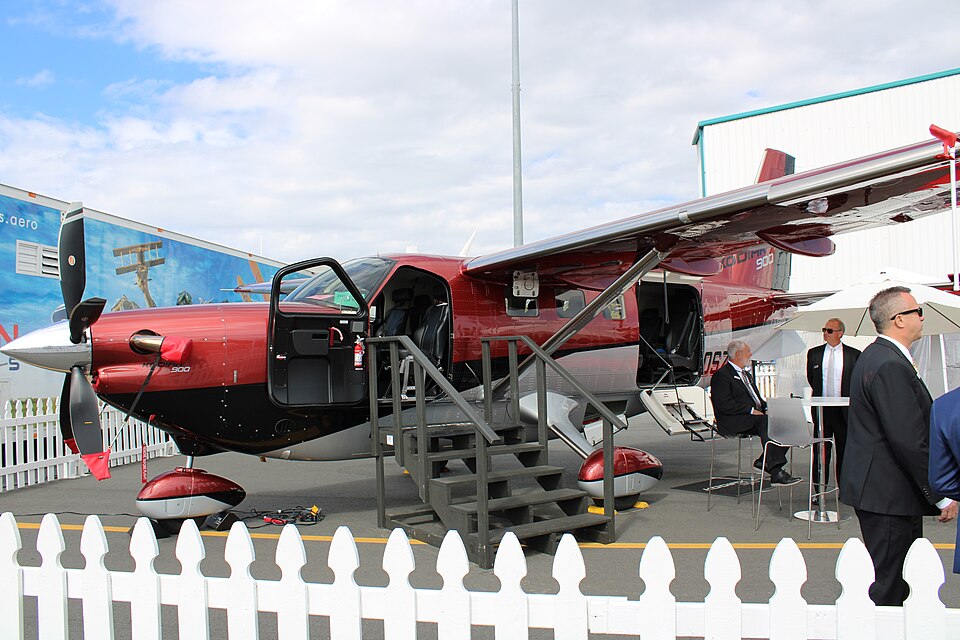 A Daher Kodiak 900 at 2022 NBAA-BACE, Orlando Executive Airport with the main door open, following steps down and 3 staff in the right corner of the photo