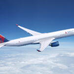 A white and red Delta Air Lines Airbus jet flying above a layer of cloud in front of a dark blue sky.