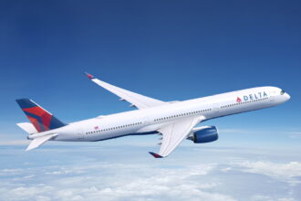 A white and red Delta Air Lines Airbus jet flying above a layer of cloud in front of a dark blue sky.