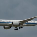 A white and blue Air China jet flying in front of a cloudy sky.