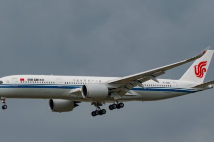A white and blue Air China jet flying in front of a cloudy sky.