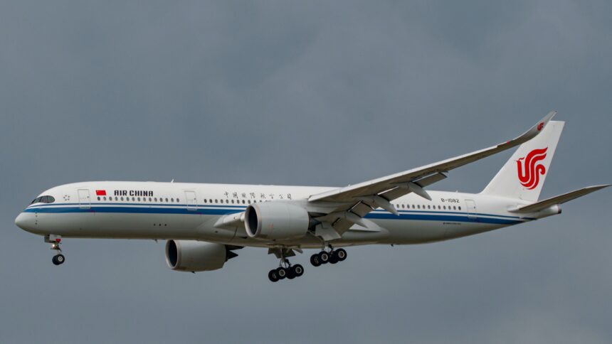 A white and blue Air China jet flying in front of a cloudy sky.