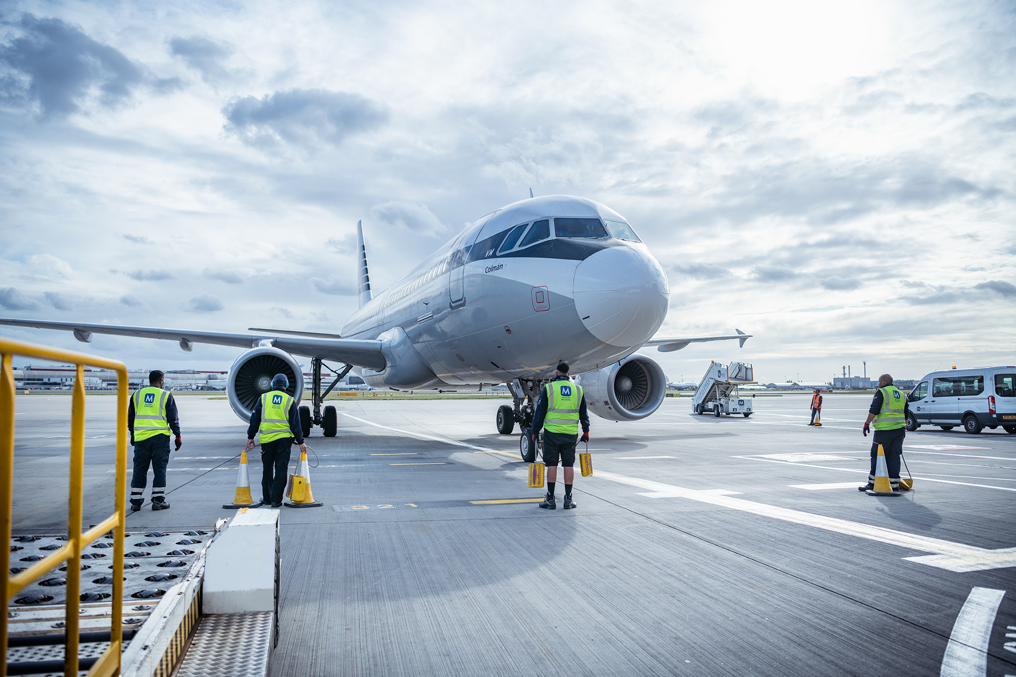 A white and grey jet being refuelled on a runway. Staff in hi-vis jackets are stood around the plane.