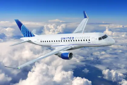 A blue and white Embraer E175 jet in the livery of United Airlines. The jet is flying over a layer of cloud.