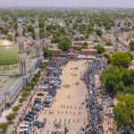 An aerial view of the city of Maiduguri in Borno, Nigeria. Pedestrians are seen walking across a wide open space next to a mosque.