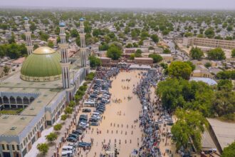 An aerial view of the city of Maiduguri in Borno, Nigeria. Pedestrians are seen walking across a wide open space next to a mosque.