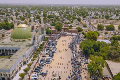 An aerial view of the city of Maiduguri in Borno, Nigeria. Pedestrians are seen walking across a wide open space next to a mosque.