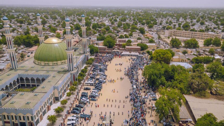 An aerial view of the city of Maiduguri in Borno, Nigeria. Pedestrians are seen walking across a wide open space next to a mosque.