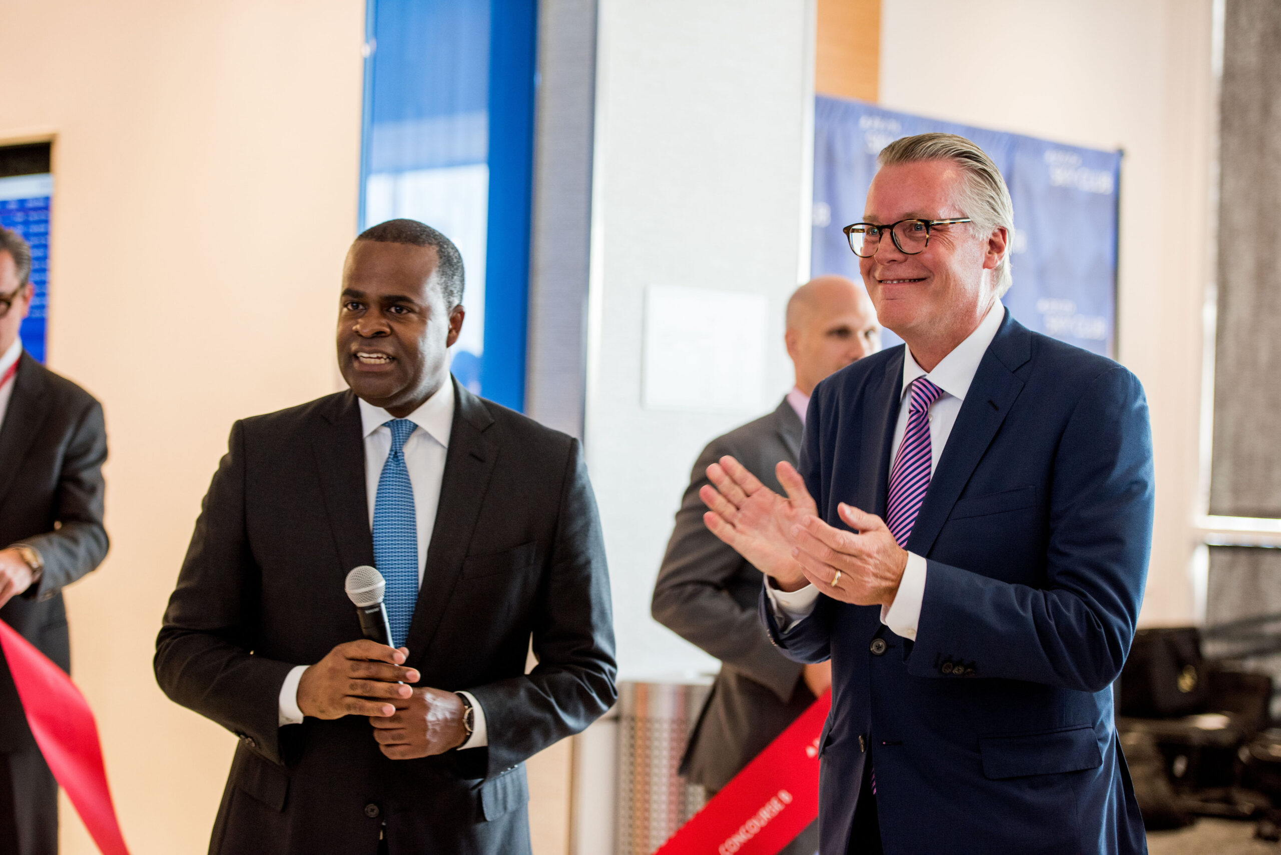 Delta CEO Ed Bastian (right) pictured alongside the Mayor of Atlanta Kasim Reed. Bastian is clapping while Reed holds a microphone.