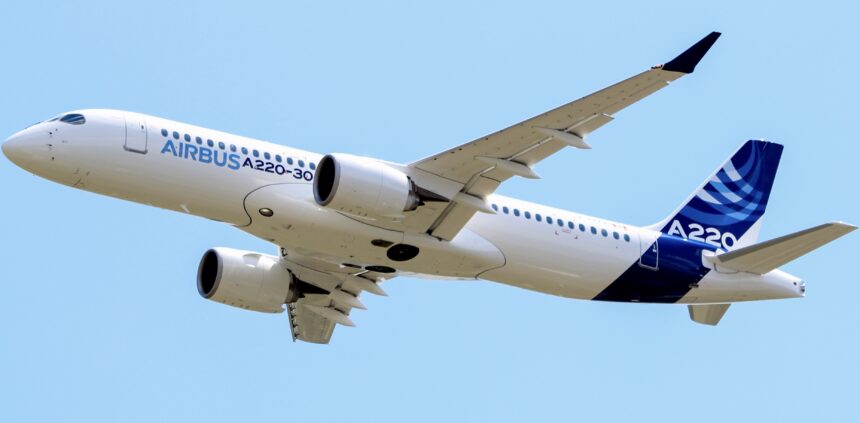 A blue and white Airbus A220-300 jet flying in front of a clear blue sky.