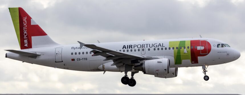 A red, white, and green, TAP Air Portugal jet flying over a building at dusk.