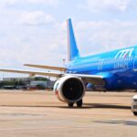 A blue ITA Airways jet sat on a runway. A small vehicle is parked next to the jet, and a cloudy sky is shown behind.