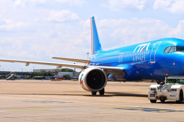 A blue ITA Airways jet sat on a runway. A small vehicle is parked next to the jet, and a cloudy sky is shown behind.