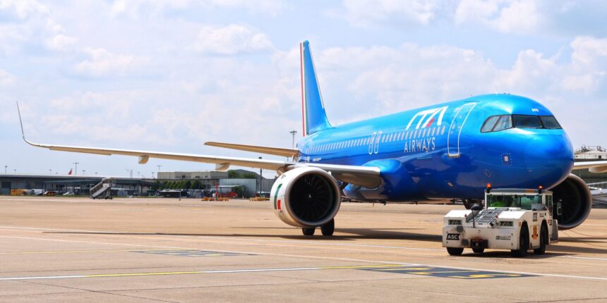 A blue ITA Airways jet sat on a runway. A small vehicle is parked next to the jet, and a cloudy sky is shown behind.