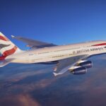 A red, white, and blue, British Airways jet flying over a layer of cloud.