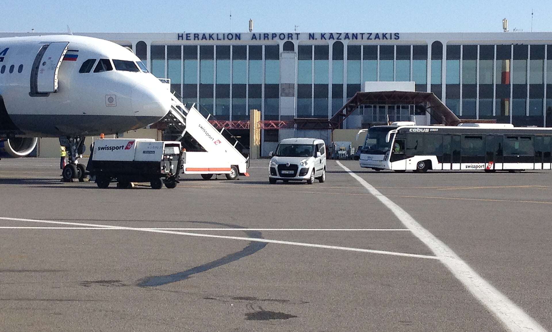 A bus, and the white nose of a jet, parked in front of the terminal building at HER, Crete.