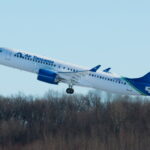 A blue and white Air Tanzania jet taking off in front of a row of trees.