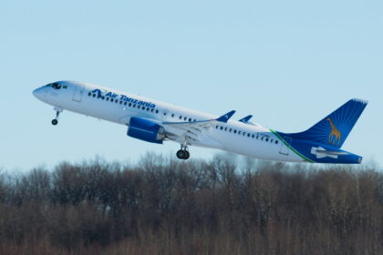 A blue and white Air Tanzania jet taking off in front of a row of trees.