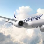 A white and blue Finnair Embraer E195-E2 jet flying in front of a cloudy sky.
