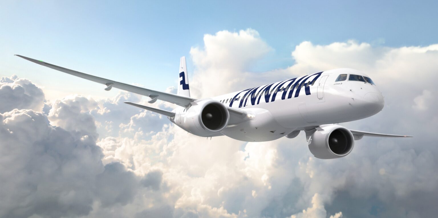 A white and blue Finnair Embraer E195-E2 jet flying in front of a cloudy sky.