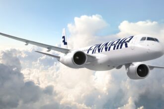 A white and blue Finnair Embraer E195-E2 jet flying in front of a cloudy sky.