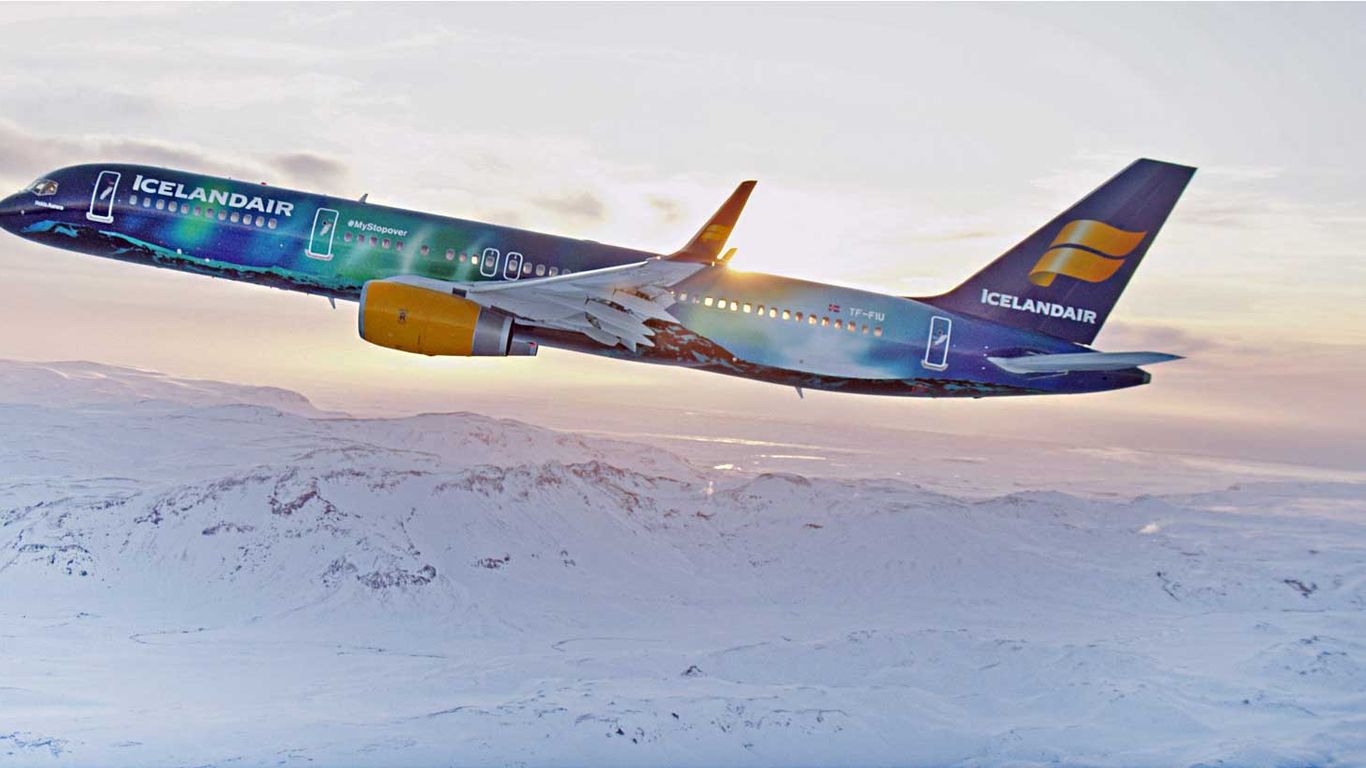 A multicoloured Icelandair jet flying over a snowy landscape at sunset.