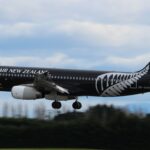 A black and white Air New Zealand jet flying above a line of dark green trees.