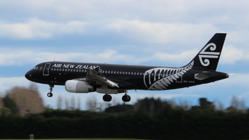 A black and white Air New Zealand jet flying above a line of dark green trees.