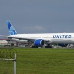 United Airlines Boeing 777 taxiing on a runway beside a fenced grass under a grey sky