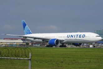 United Airlines Boeing 777 taxiing on a runway beside a fenced grass under a grey sky