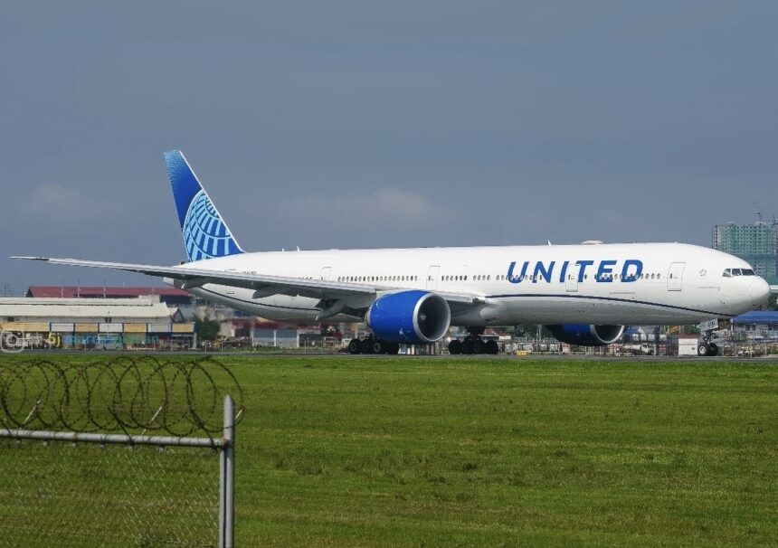 United Airlines Boeing 777 taxiing on a runway beside a fenced grass under a grey sky