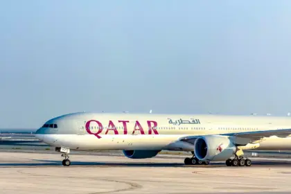 Qatar Airways Boeing 777 taxiing on a wide concrete apron under a clear, pale blue sky