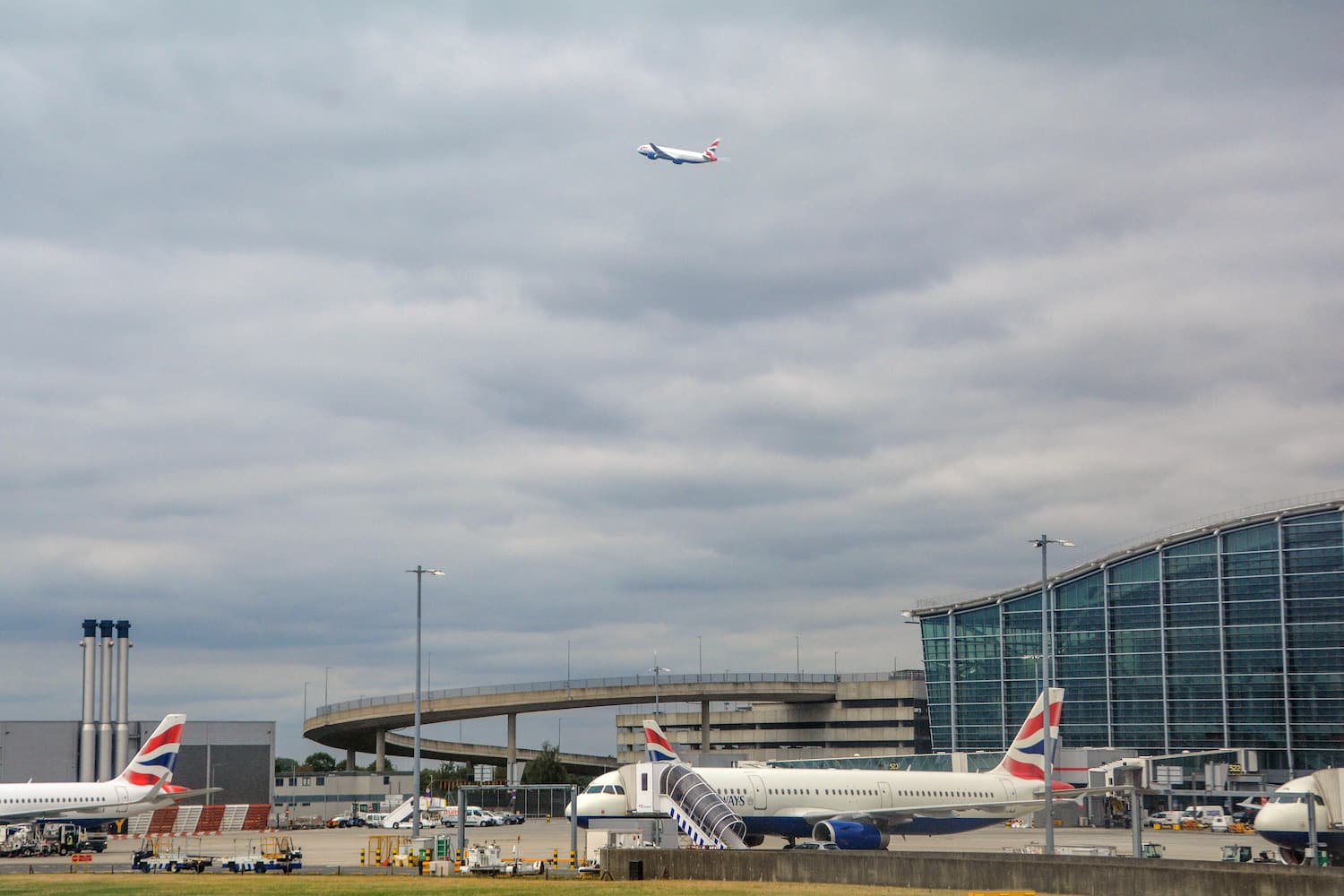 Image shows exterior of Heathrow Airport with a British Airways plane in the foreground and another taking off in the background.
