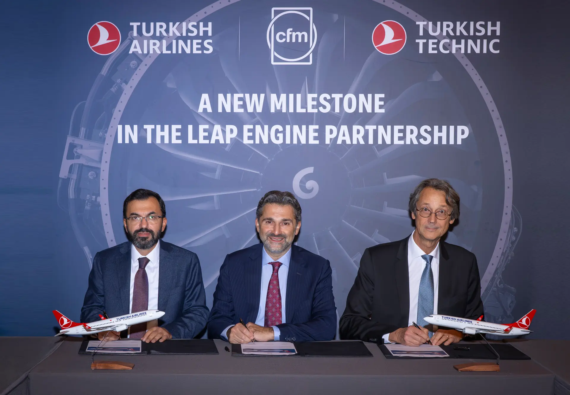 Three men in suit signing documents at a table in front of a Turkish Airlines, CFM and Turkish Technic backdrop.