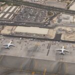 An outside aerial image of Mumbai International Airport, Terminal 2. The surroundings are dull and dry with a few airplanes dotted along the outside.