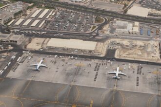 An outside aerial image of Mumbai International Airport, Terminal 2. The surroundings are dull and dry with a few airplanes dotted along the outside.