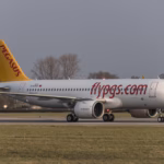 Pegasus Airlines Airbus A320neo in white livery with a yellow tail and "flypgs.com" on the fuselage, on a runway with grass in the foreground.