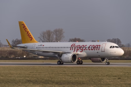 Pegasus Airlines Airbus A320neo in white livery with a yellow tail and "flypgs.com" on the fuselage, on a runway with grass in the foreground.