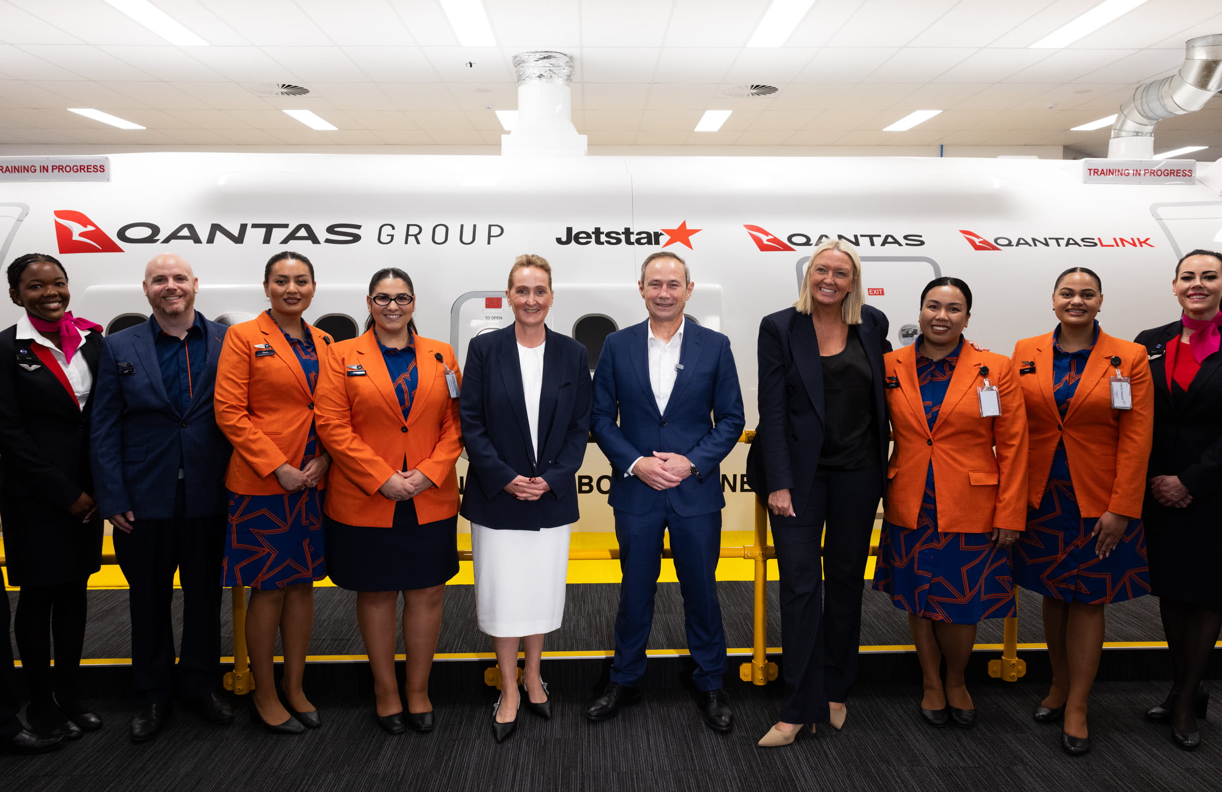 Staff of Qantas Group pictured smiling, lined up against a training centre in the back.