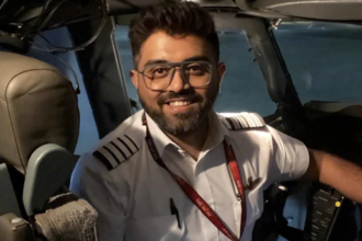 Image shows Smit Machcchar in the cockpit of a plane, smiling at the camera. He has dark hair and a beard, wearing a pilot's uniform and glasses.