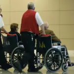 Two people pushing two people in wheelchairs at an airport.