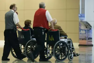 Two people pushing two people in wheelchairs at an airport.