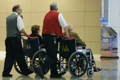 Two people pushing two people in wheelchairs at an airport.