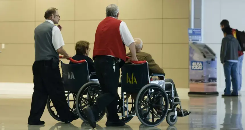 Two people pushing two people in wheelchairs at an airport.