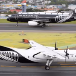 Two Air New Zealand aircraft on airport taxiways, including a De Havilland Q300 turboprop in the foreground and an Airbus narrowbody aircraft in the background, with airport buildings and residential areas visible beyond the airfield.