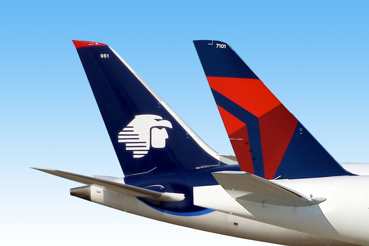 Photograph shows two commercial airplane tail sections side by side against a clear blue sky, highlighting airline branding and livery designs. Left tail features dark navy, red, and white colors with a stylized logo and identifier “961,” while right tail displays Delta-style red and navy geometric markings with identifier “7101.”