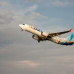 flydubai plane overhead with clouds appearing against a blue sky in the background.