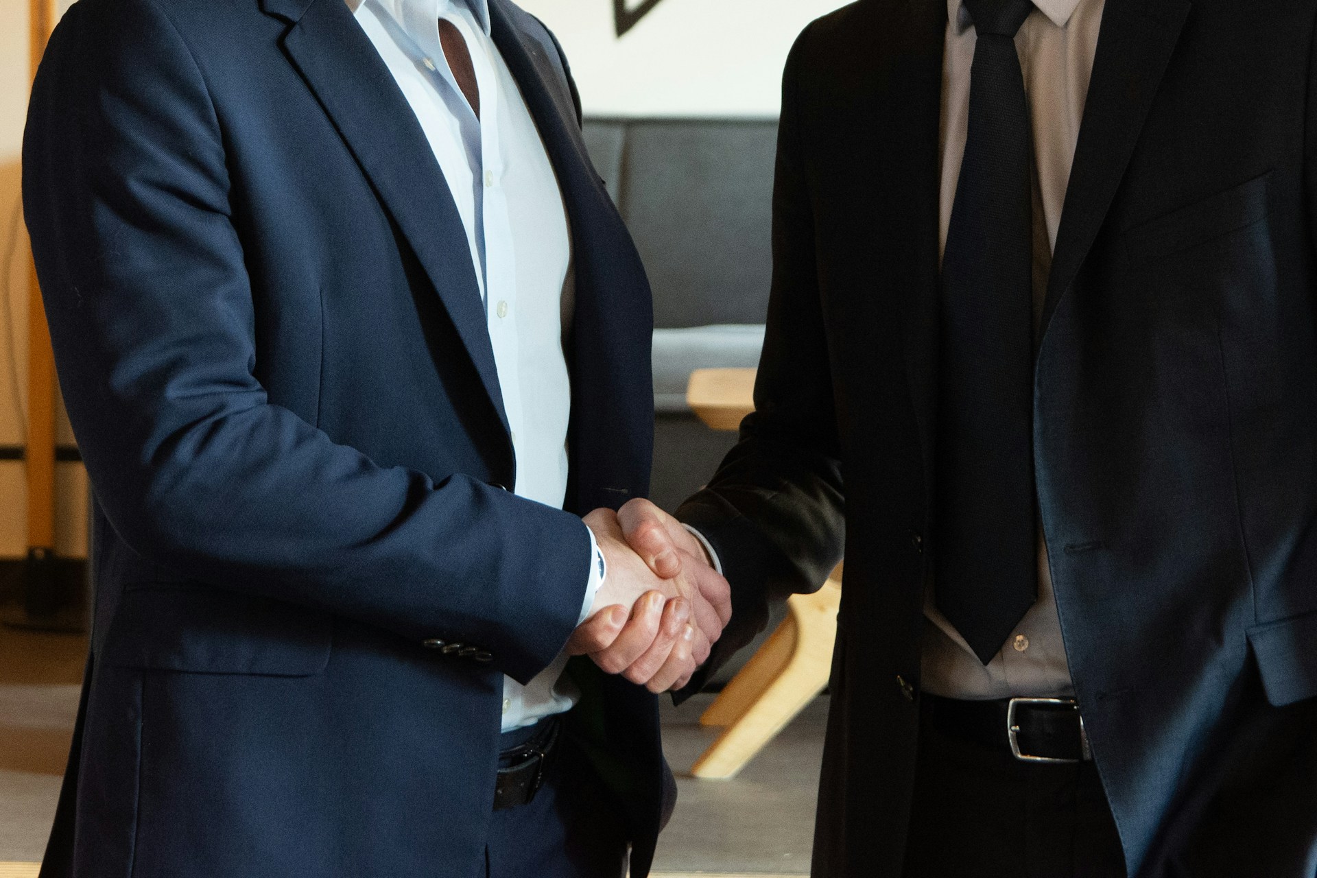 Two people are pictured wearing suits and ties, and shaking hands. Their faces are cropped out of the image.