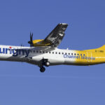 An Aurigny Air Services plane ascending into a bright blue sky.